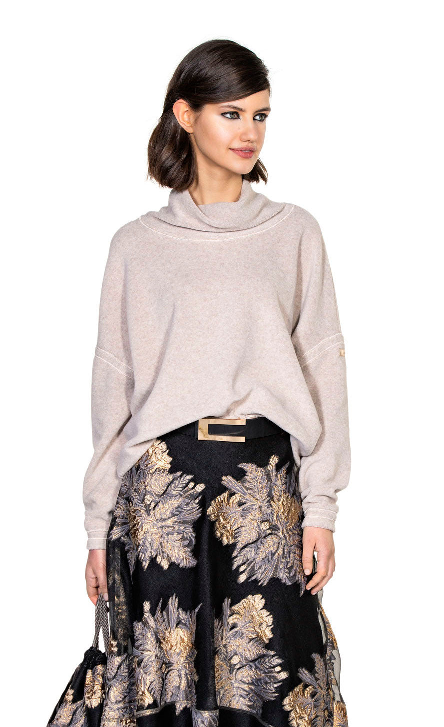Front top half view of a woman wearing a skirt and the beate heymann cozy sweatshirt in the color nature. This color is cream/beige. The sweatshirt has drop shoulder long sleeves and a cowl neck.