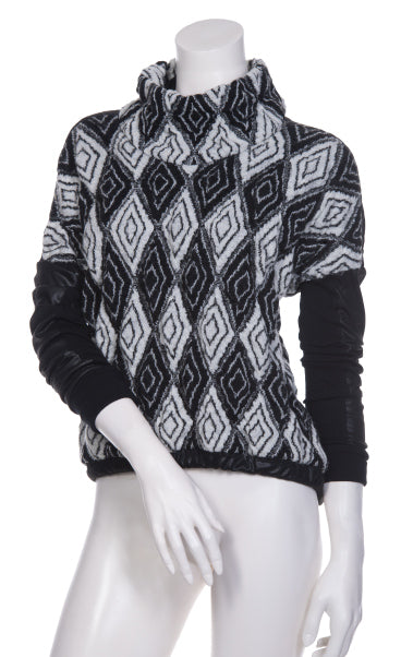 Front top half view of the beate heymann knit rhombus top. This top has a black and white diamond/rhombus print with a mock neck and drop shoulder leather-looking black long sleeves.