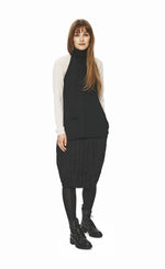 Load image into Gallery viewer, Front full body view of a woman wearing the bitte kai rand wool front piece in black over a white top and with a black skirt. This front piece has a single front pocket on the bottom right side, no sleeves, and a turtleneck.
