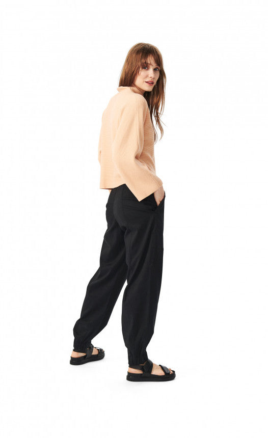 Back, right sided full body view of a woman wearing the bitte kai rand botanic twill elastic pant. This pant is black and has a relaxed fit with an elastic hem.