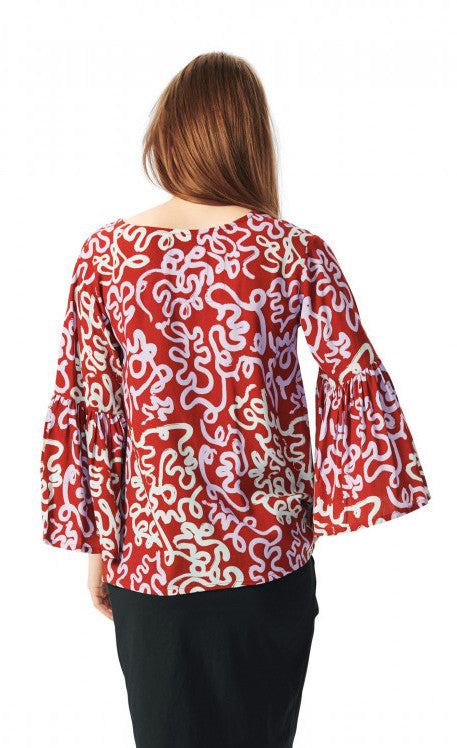 Back top half view of a woman wearing the bitte kai rand dancing brush blouse. This top is red with a pastel purple and pastel green swirl print. The top also has ruffled sleeves.