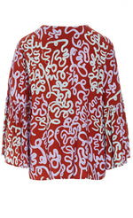Load image into Gallery viewer, Back view of the bitte kai rand dancing brush blouse. This top is red with a pastel purple and pastel green swirl print. The top has ruffled sleeves.

