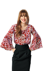 Front top half view of a woman wearing the bitte kai rand dancing brush blouse. This top is red with a pastel purple and pastel green swirl print. The top has a round neck and ruffled sleeves.
