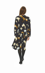Load image into Gallery viewer, Back full body view of a woman wearing the bitte kai rand falling leaves dress. This dress is dark grey with mustard and light blue colored leaves all over. The dress has long sleeves and a seam at the waist.
