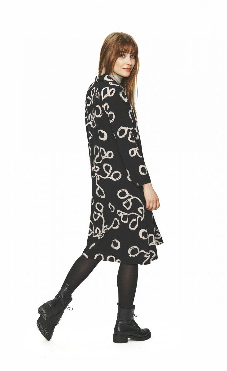 Back full body view of a woman wearing tights and the bitte kai rand lunaria shirt dress. This dress is black with long sleeves and a cream squiggle print.