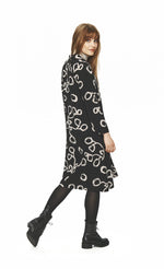 Load image into Gallery viewer, Back full body view of a woman wearing tights and the bitte kai rand lunaria shirt dress. This dress is black with long sleeves and a cream squiggle print.
