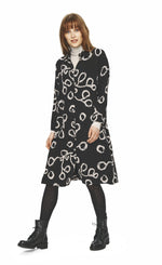 Load image into Gallery viewer, Front full body view of a woman wearing tights and the bitte kai rand lunaria shirt dress. This dress is a black button down dress with long sleeves and a cream squiggle print.
