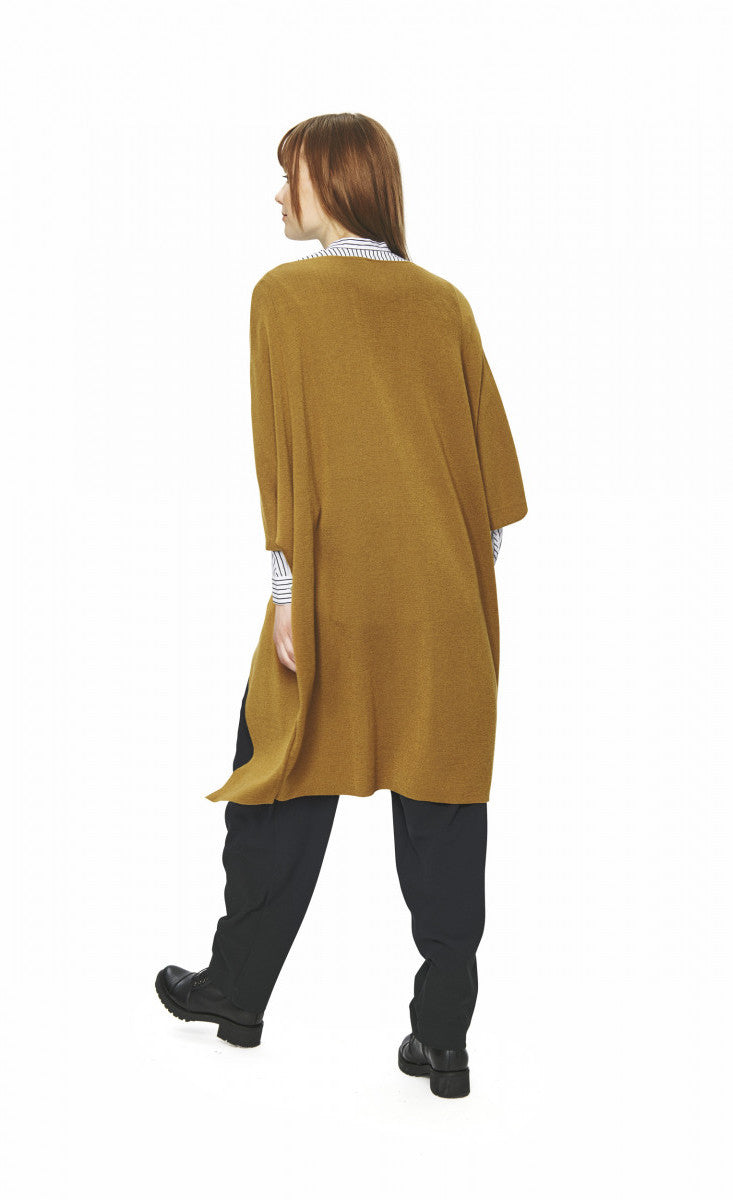 back full body view of a woman wearing black pants, a black and white shirt and the bitte kai rand merino mix cape in the color mustard. This cape has two wide elbow length sleeves and sits below the hips.