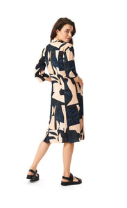 Back full body view of a woman wearing the bitte kai rand monstera wrap dress. This dress is nude with black and blue abstract print on it. The dress has 3/4 length sleeves and ends at the knees.