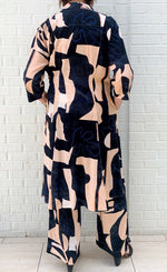 Load image into Gallery viewer, Back full body view of a woman wearing the bitte kai rand monstera wrap dress with the bitte kai rand monstera pant. These dress and pants are nude with black and blue abstract print on them. The dress has a tie and ends at the knees.
