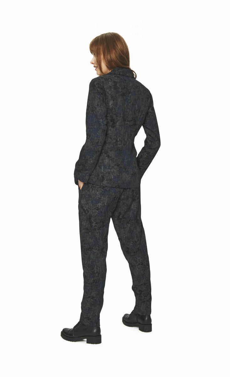 Back full body view of a woman wearing the bitte kai rand night cloud blazer jacket. This jacket has a mixed print of black and navy and long sleeves.