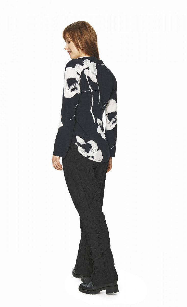 back full body view of a woman wearing black pants and the bitte kai rand oki flower shirt. This shirt is black with large white flowers. It has long sleeves, and a form-fitting silhouette.