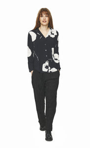 Front full body view of a woman wearing black pants and the bitte kai rand oki flower shirt. This shirt is black with large white flowers. It has a button down front, long sleeves, and a form-fitting silhouette.