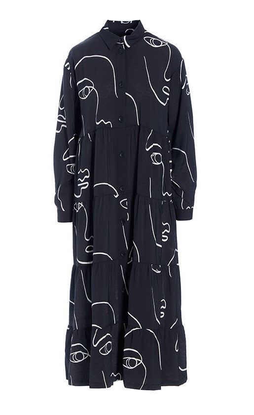 Front view of the bitte kai rand sketch viscose long dress. This dress is black with white sketches of faces all over it. The dress has a button up front, a collar, long sleeves, and a ruffled bottom half.