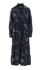 Load image into Gallery viewer, Front view of the bitte kai rand sketch viscose long dress. This dress is black with white sketches of faces all over it. The dress has a button up front, a collar, long sleeves, and a ruffled bottom half.
