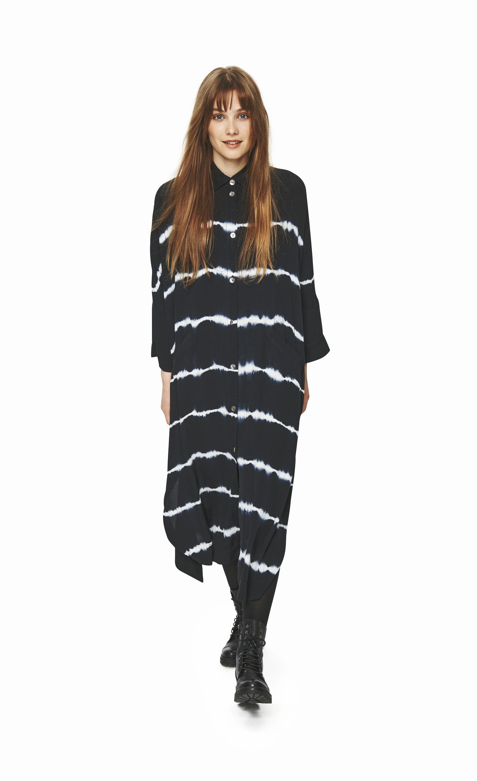 Front full body view of a woman wearing the bitte kai rand suki shibori shirt dress. This long dress is black with tie-dyed lines. It has long sleeves and a button down front.