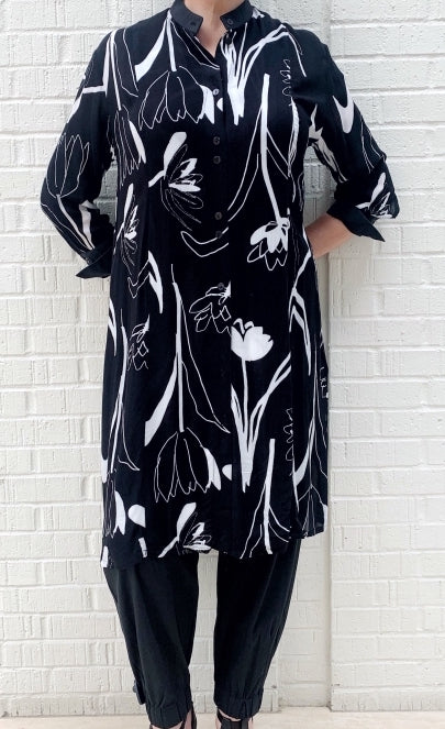 Front full body view of a woman wearing the bitte kai rand tulip tango shirt dress. This dress is black with black and white tulip flowers all over it. The dress has a button up front and 3/4 length sleeves. It ends at the knees.