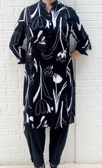 Load image into Gallery viewer, Front full body view of a woman wearing the bitte kai rand tulip tango shirt dress. This dress is black with black and white tulip flowers all over it. The dress has a button up front and 3/4 length sleeves. It ends at the knees.
