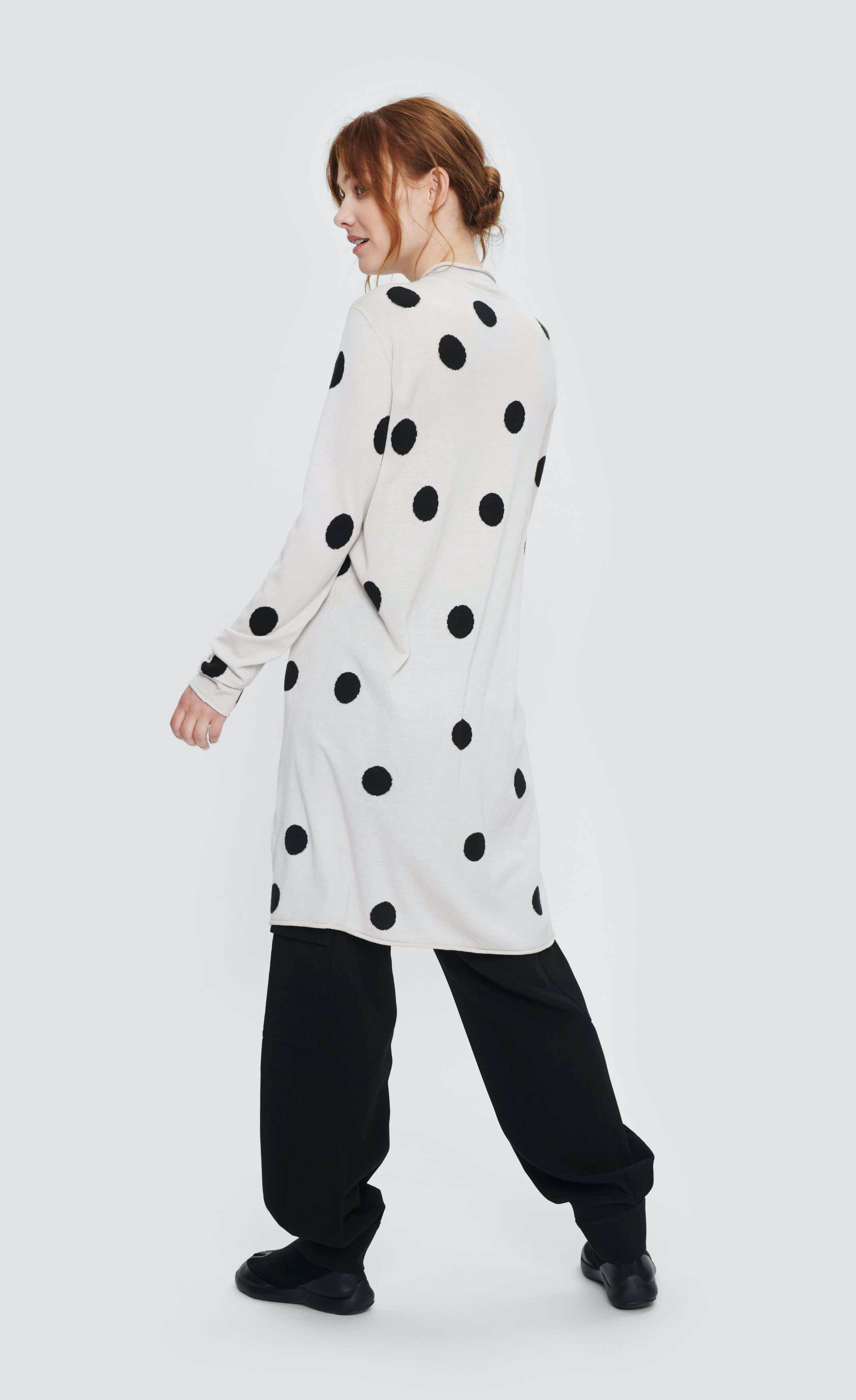 Back full body view of a woman wearing the bitte kai rand floret knit tunic with dots. This tunic is in the color white with black dots. It has long sleeves and sits at the knees.