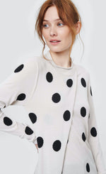 Load image into Gallery viewer, Front top half view of a woman wearing the bitte kai rand floret knit tunic with dots. This tunic is in the color white with black dots. It has a wrapped feature in the front that closes at the neck. 
