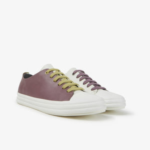 Outer side front view of a pair of the camper twins sneaker. The left sneaker is white on one side and grey on the other with purple laces. The right foot is white on one side and purple on the other side with mustard laces.