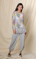 Load image into Gallery viewer, Front full body view of a woman wearing the chalet andrea basic top. This top has long sleeves, a round neck, crinkled fabric, and a multicolored patchwork print. The model is wearing grey capris.
