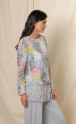 Load image into Gallery viewer, Front, right side, top half view of a woman wearing the chalet andrea basic top. This top has long sleeves, a round neck, crinkled fabric, and a multicolored patchwork print.
