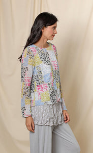 Front, right side, top half view of a woman wearing the chalet andrea basic top. This top has long sleeves, a round neck, crinkled fabric, and a multicolored patchwork print.