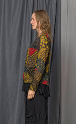 Load image into Gallery viewer, left side top half view of a woman wearing the chalet andrea patch top. This top has long sleeves, a round neck, and a relaxed fit. The top has a mix of yellow, brown, and red print.
