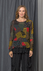 front top half view of a woman wearing the chalet andrea patch top. This top has long sleeves, a round neck, and a relaxed fit. The top has a mix of yellow, brown, and red print.