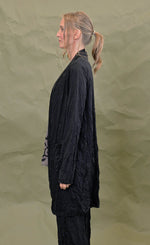 Load image into Gallery viewer, left side top half view of a woman wearing the chalet black cleon cardigan. This long cardigan has long sleeves, a draped open front, and front draped pockets.
