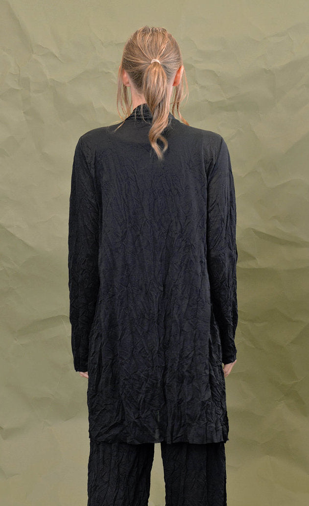 back top half view of a woman wearing the chalet black cleon cardigan. This long cardigan has long sleeves, a draped open front, and two front draped pockets.