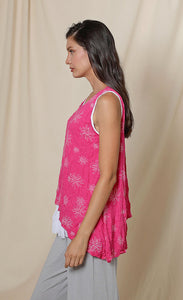 Left side top half view of a woman wearing the chalet eleanor tank. This tank is fuschia pink with white flowers on it. The tank has an asymmetrical hem with a longer left side.