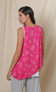 Back top half view of a woman wearing the chalet eleanor tank. This tank is fuschia pink with white flowers on it. The tank has an asymmetrical hem with a longer left side.