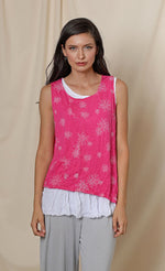 Load image into Gallery viewer, Front top half view of a woman wearing the chalet eleanor tank. This tank is fuschia pink with white flowers on it. The front has a small patch pocket on the right side. The tank has an asymmetrical hem with a longer left side.
