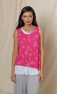 Front top half view of a woman wearing the chalet eleanor tank. This tank is fuschia pink with white flowers on it. The front has a small patch pocket on the right side. The tank has an asymmetrical hem with a longer left side.