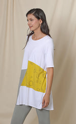 Load image into Gallery viewer, Front left sided top half view of a woman wearing the chalet fallon tunic. This tunic is white with a yellow patch and a grey patch pocket in the front. This tunic sits below the hips.
