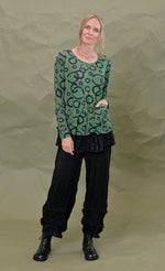 Load image into Gallery viewer, Front full body view of a woman wearing the chalet gizel top in treetop. This top is green colored with black circles. It has long sleeves, a round neck, and a front patch pocket.
