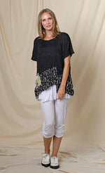 Load image into Gallery viewer, Front full body view of a woman wearing the chalet josephine top. This short sleeve top is black with a black and white print band at the bottom and a patchwork printed front pocket.
