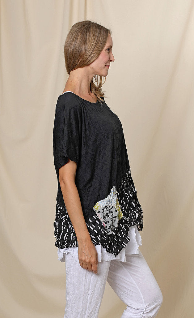 Right side top half view of a woman wearing the chalet josephine top. This short sleeve top is black with a black and white print band at the bottom and a patchwork printed front pocket.
