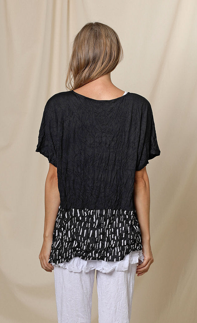 Back top half view of a woman wearing the chalet josephine top. This short sleeve top is black with a black and white printed band at the bottom.