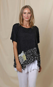 Front top half view of a woman wearing the chalet josephine top. This short sleeve top is black with a black and white print band at the bottom and a patchwork printed front pocket.
