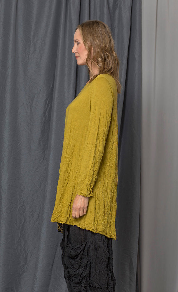 Left side top half view of a woman wearing the chalet katya top in the color medallion (yellow). This top is a tunic with long sleeves, a round neck, and an asymmetrical hem.