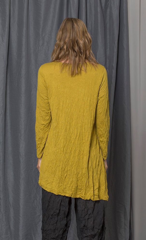 Back top half view of a woman wearing the chalet katya top in the color medallion (yellow). This top is a tunic with long sleeves, a round neck, and an asymmetrical hem.