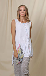 Load image into Gallery viewer, Front top half view of a woman wearing the chalet lucianna tunic. This tunic is sleeveless. It is white with multicolored patchwork trim and a front draped multicolored patchwork pocket. The tunic has an asymmetrical hem. 
