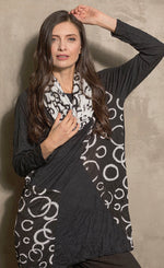 Load image into Gallery viewer, Front top half view of a woman wearing black pants and the chalet onyx pippa tunic. This black tunic has long sleeves, patches of white circle print and a pocket with the same print on it.
