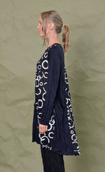Load image into Gallery viewer, Left side top half view of a woman wearing black pants and the chalet onyx pippa tunic. This black tunic has long sleeves and patches of white circle print.
