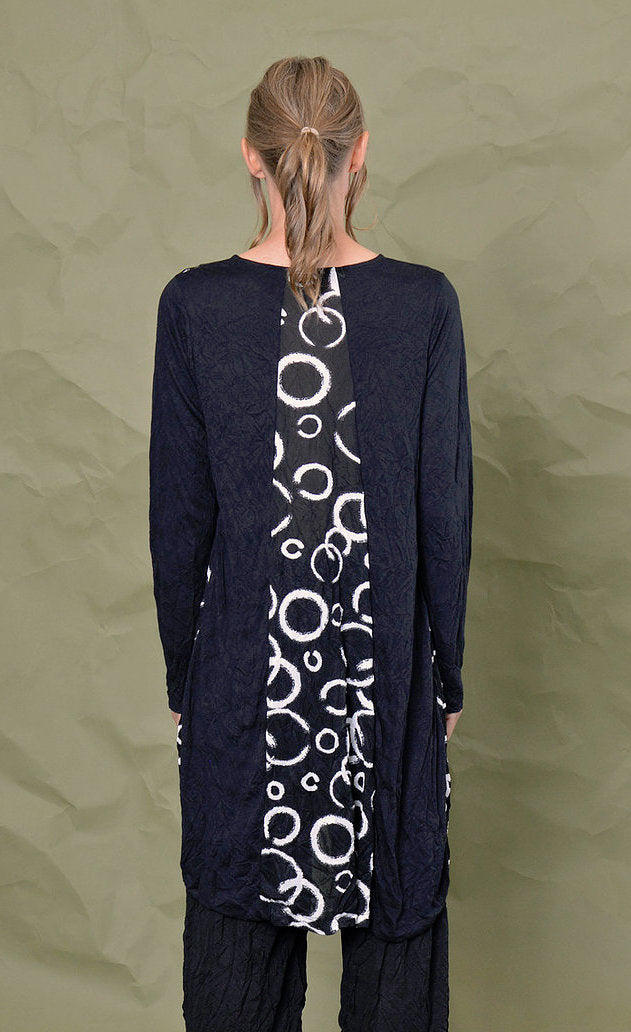 Back top half view of a woman wearing black pants and the chalet onyx pippa tunic. This black tunic has long sleeves and a patch of white circle print down the middle.