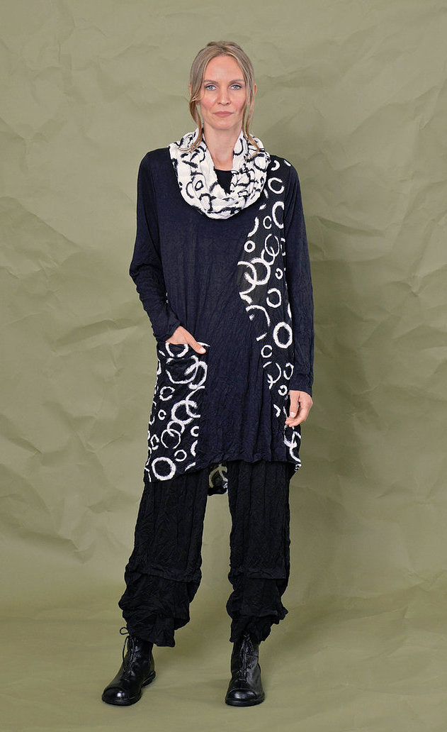 Front full body view of a woman wearing black pants and the chalet onyx pippa tunic. This black tunic has long sleeves, patches of white circle print and a pocket with the same print on it. The model has her hand in the front pocket.