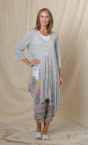 Front full body view of a woman wearing the chalet orla jacket. The jacket in this image is grey with a patchwork print on the right side, a 3 button front, 3/4 length sleeves, and an asymmetrical hem.